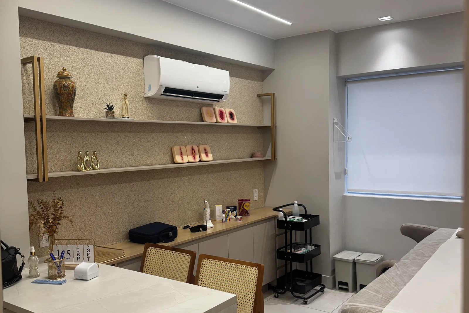 Sala de atendimento da clínica, com bancada, maca e carrinho de materiais